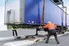 Zwei Arbeiter positionieren einen Wechselaufbau auf einem Anhänger.