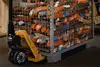 Gitterbox mit orangefarbenen Zurrgurten, bewegt mit einem Hubwagen in einem Lagerbereich.