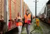 Two apprentices in safety vests standing beside freight wagons in a rail yard