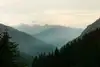 Neblige Alpenlandschaft mit gestaffelten Berggipfeln und bewaldetem Tal im Abendlicht