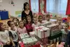 Lehrerin und Kinder im Klassenraum versammelt um einen Tisch mit eingepackten Weihnachtsgeschenken