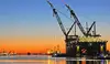 Hafen Rotterdam bei Sonnenuntergang mit großem Kranschiff und Windrädern im Hintergrund
