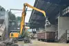 Bagger mit Greifer lädt Metallschrott in einen offenen Güterwagen in einer Recyclinganlage