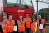 Mitarbeitende der Rail Cargo Group mit Sicherheitswesten vor einer roten ÖBB-Lokomotive an einer Bahnstrecke