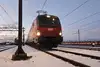 Rote ÖBB Vectron-Elektrolok im verschneiten Rangierbahnhof bei Dämmerung, mit Scheinwerfern.
