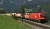 Güterzug der ÖBB Rail Cargo Group fährt auf elektrifizierter Strecke durch eine Berglandschaft.