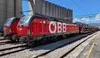 ÖBB-Lokomotive mit Autotransportwagen der Rail Cargo Group vor einer Industrieanlage.