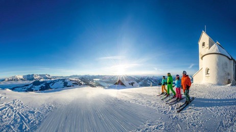 3 Skifahrer vor verschneiter Kapelle