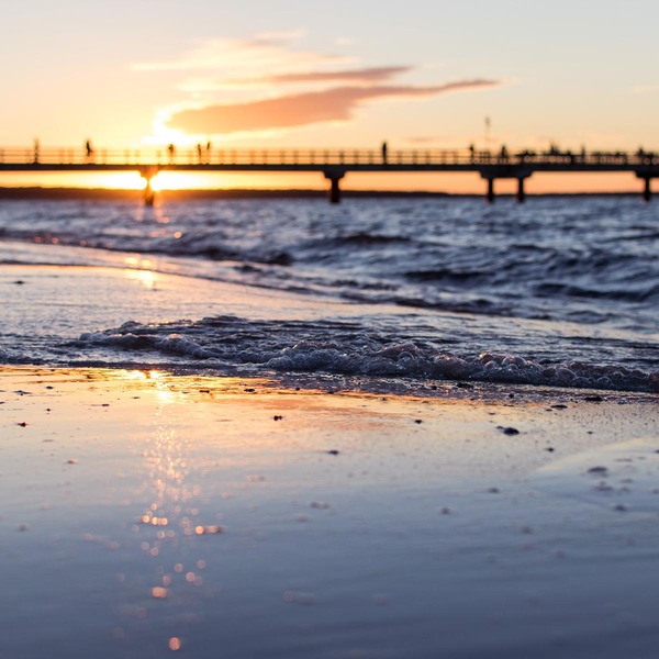 Sonnenuntergang am Meer, im Hintergrund sieht man eine Brücke mit Menschen