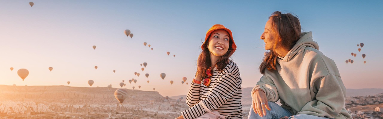 Zwei Personen sitzen vor Himmel voller Heißluftballons