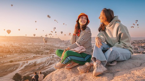 Zwei Personen sitzen vor Himmel voller Heißluftballons